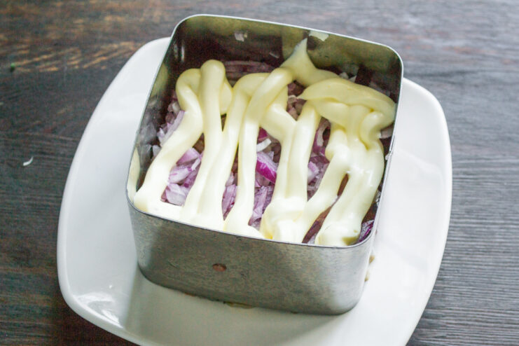 Using Mayonnaise to Bind the Salad Layers Spreading a layer of mayonnaise over the onion layer inside a food ring.