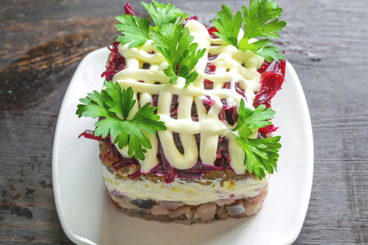 Garnishing the Finished Herring Under a Fur Coat Salad The finished Seledka pod shuboy salad, perfectly layered in a ring and garnished with fresh parsley.