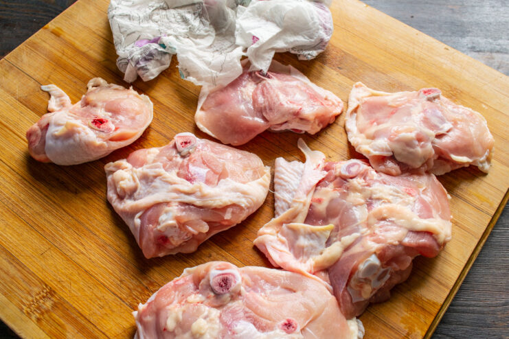 How to Debone Chicken Thighs for Skewers A person deboning a chicken thigh with a sharp knife on a cutting board.