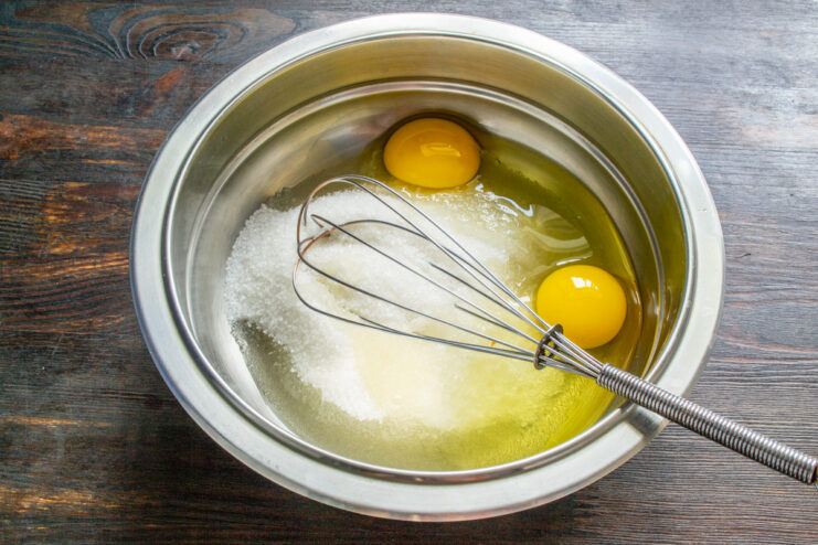 Step 1: Combining sugar and eggs for the muffin batter A glass bowl containing granulated sugar and two cracked eggs, ready for mixing.