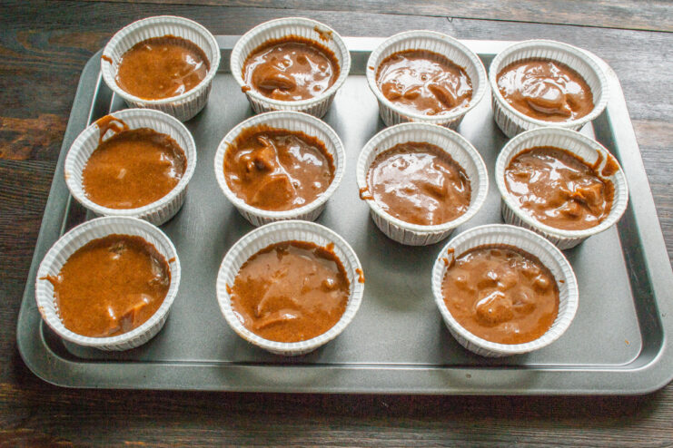 Step 7: Portioning the muffin batter into paper liners Filling paper muffin liners in a muffin tin with chocolate peach batter.