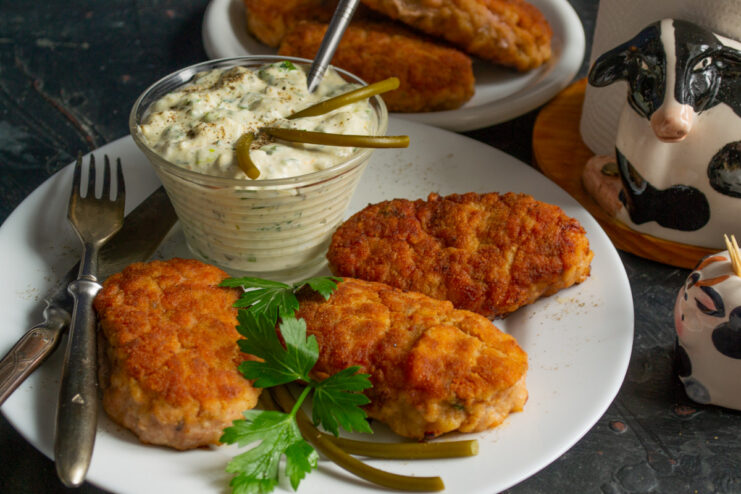 Plate of juicy kotlety (meat patties) served with a side of tartar sauce and garnished with herbs.