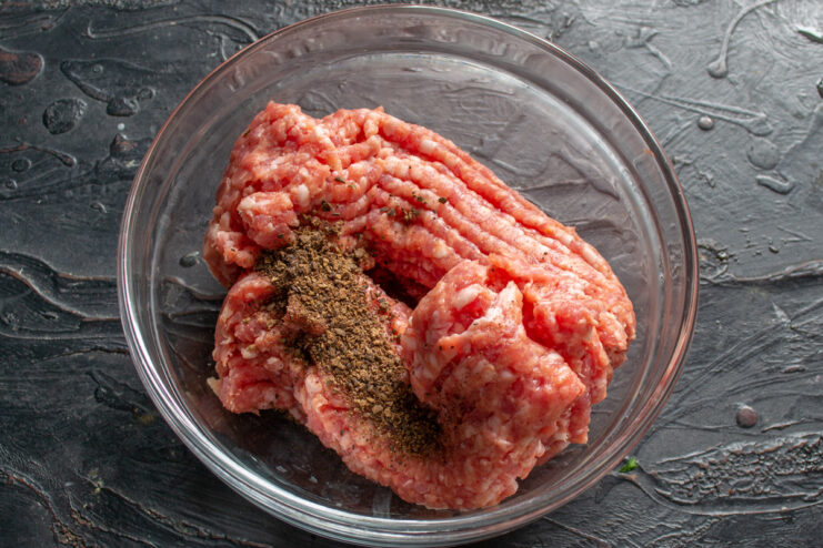 Seasoning Ground Meat for Flavorful Kotlety A bowl of ground beef and pork mix being seasoned with freshly ground allspice for making kotlety.