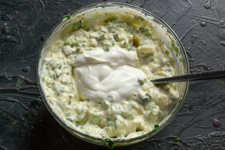 Combining All Ingredients for a Creamy Tartar Sauce A spoon mixing all the ingredients for tartar sauce in a white bowl until well combined.