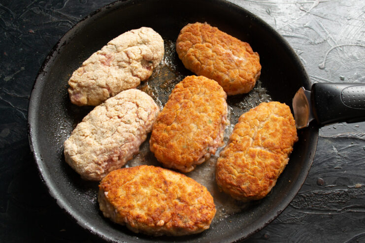 Searing Kotlety for a Golden-Brown Crust Several breaded kotlety (meat patties) sizzling in a hot skillet with oil.