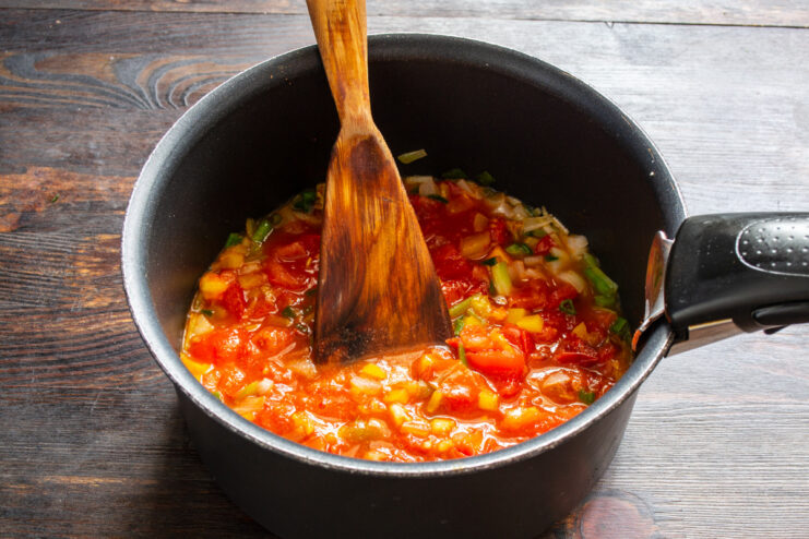 Seasoning the Tomato Sauce with Spices A teaspoon of sweet paprika being added to the tomato sauce in a pan.
