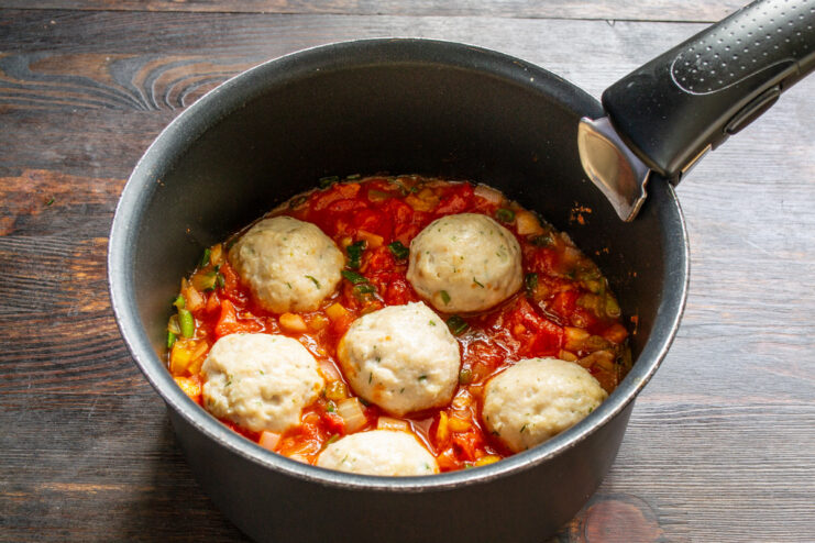 Combining Meatballs with the Tomato Sauce Cooked chicken meatballs being added to the simmering tomato sauce in a pan.