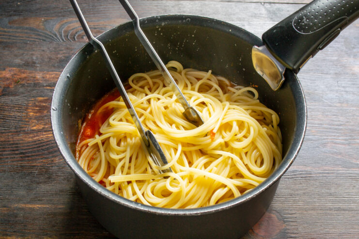 Tossing Cooked Spaghetti with Sauce and Meatballs Cooked spaghetti being transferred into the sauté pan with tomato sauce and meatballs.