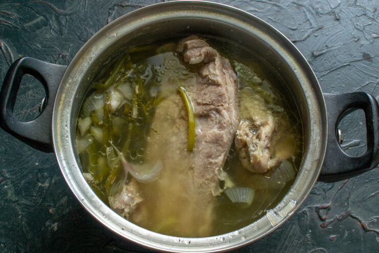 Simmering pork ribs to create a rich and flavorful soup broth A pot of pork ribs simmering in water with spices, with foam being removed by a skimmer.