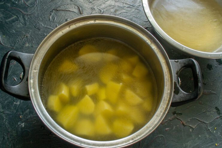 Pouring the clear, strained pork broth over the potatoes Strained, clear broth being poured into a pot with potatoes.