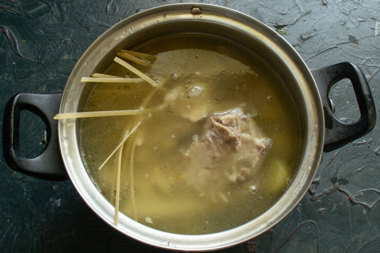 Adding noodles and cooked ribs to the boiling potato soup Noodles and cooked pork ribs being added to the pot of boiling soup.