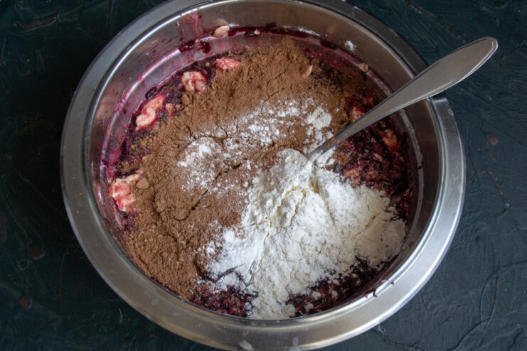 Adding Dry Ingredients: Flour and Cocoa Powder Sifting flour and cocoa powder into the wet brownie batter.