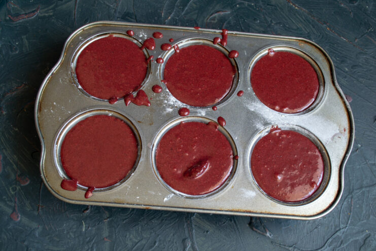 Portioning the Brownie Batter into Muffin Tins Pouring the dark red brownie batter into a prepared muffin tin.
