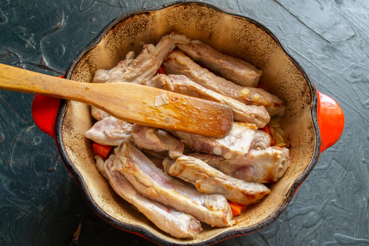 Layering the Ingredients in the Pot Golden-brown seared pork ribs layered over a bed of cooked carrots and onions in a pot.