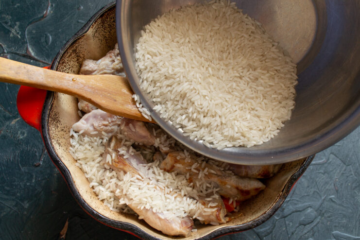 Adding Rice to the Dutch Oven Uncooked long-grain rice being poured over pork ribs and vegetables in a Dutch oven.