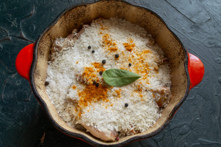 Seasoning the Dish with Turmeric for Color and Flavor A hand sprinkling yellow ground turmeric over the rice and ribs in the pot.