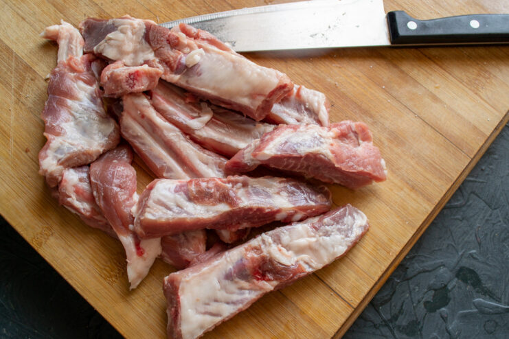 How to Prepare Pork Ribs for Cooking A rack of meaty pork ribs being cut into single pieces on a wooden board.