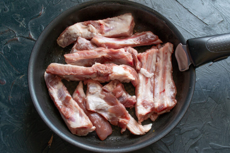 Searing the Pork Ribs to a Golden Brown Individual pork ribs being placed into a hot skillet to sear.