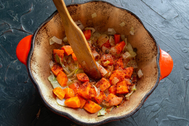 Combining Sautéed Carrots and Onions Sautéed carrots being added to a pot of translucent cooked onions.