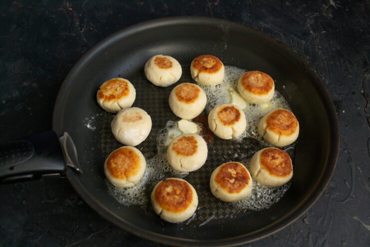 Frying Syrniki to a Golden Brown Several ricotta syrniki frying in a hot skillet until golden.