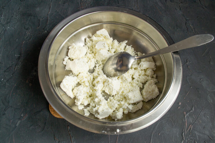 Sifting Farmer's Cheese for Smooth Syrniki Dough Fresh farmer's cheese being pushed through a metal sieve into a bowl.
