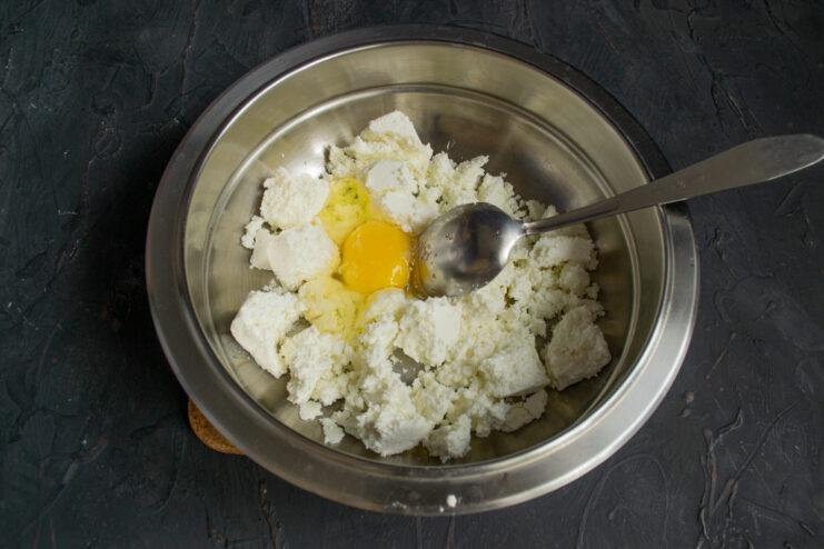 Adding an Egg to the Syrniki Mixture A hand cracking an egg into a bowl with sifted farmer's cheese.