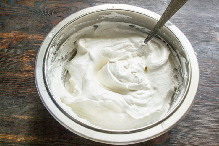 Folding Ingredients into the Meringue A spatula gently folding flour and starch into the whipped meringue filling.