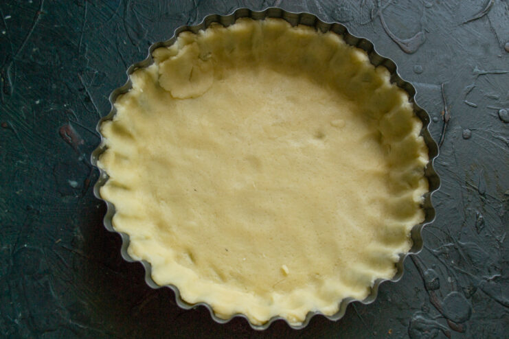 How to Easily Line a Tart Pan with Pastry Rolled-out pastry dough being carefully transferred from a rolling pin into a tart pan.