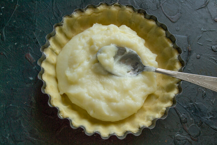 Filling the Pastry Case with Cool Custard Cooled custard being spread evenly inside the unbaked shortcrust pastry shell.