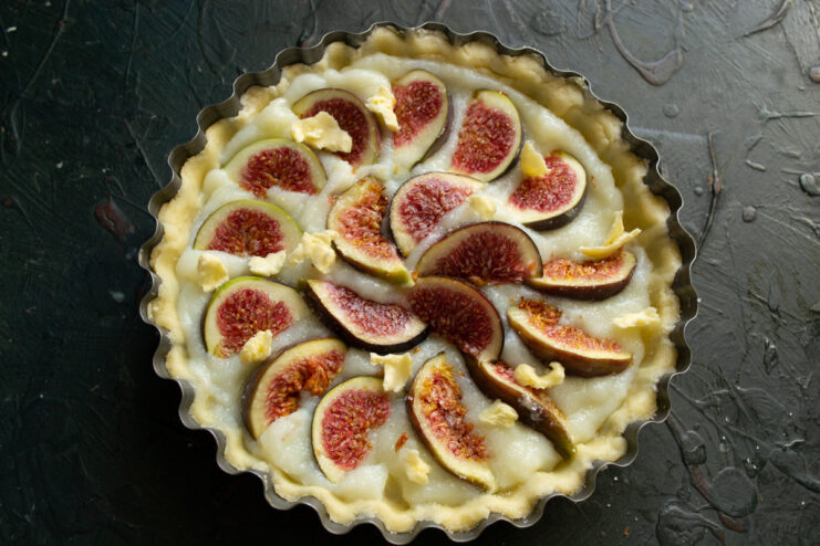 A Final Sprinkle of Sugar for Caramelization The assembled tart with figs and custard being sprinkled with sugar before baking.