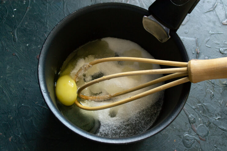 Starting the Custard Base with Sugar and Egg A saucepan with sugar and a cracked egg inside, ready for mixing.