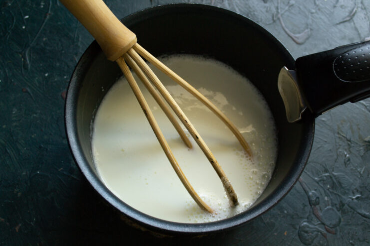 Adding Cold Cream for a Rich Custard Cold heavy cream being poured into the egg and sugar mixture in a saucepan.