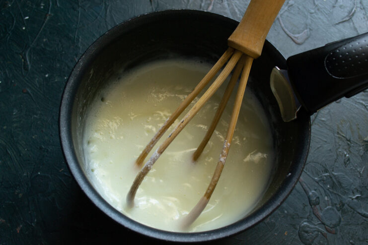 Whisking Custard Continuously Over Heat A hand whisking a creamy custard in a saucepan as it thickens on the stove.
