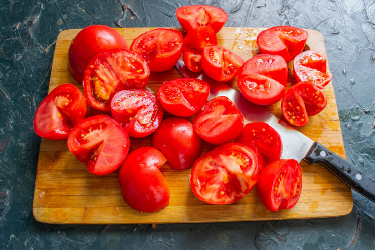How to Core Tomatoes for Sauce: Removing the Stem End Close-up of hands using a knife to core a halved red tomato.