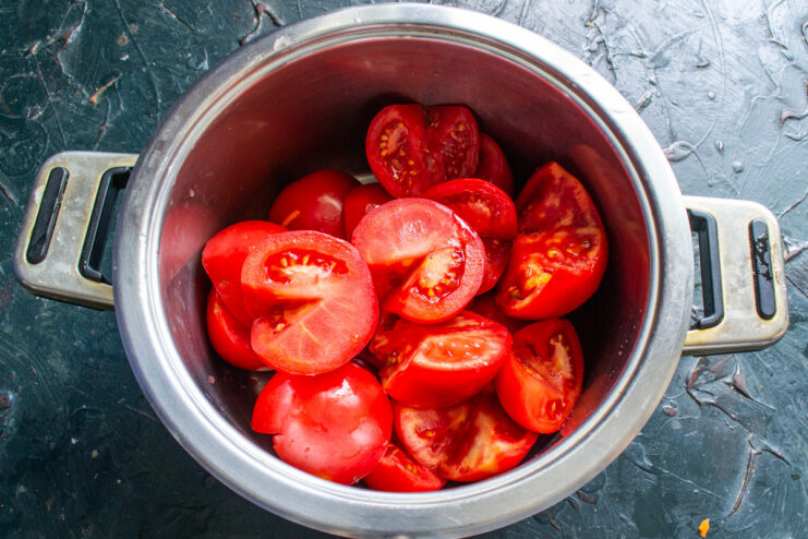 Starting the Tomato Sauce: Add Water to Prevent Sticking A large pot filled with halved tomatoes, with a small amount of water at the bottom.