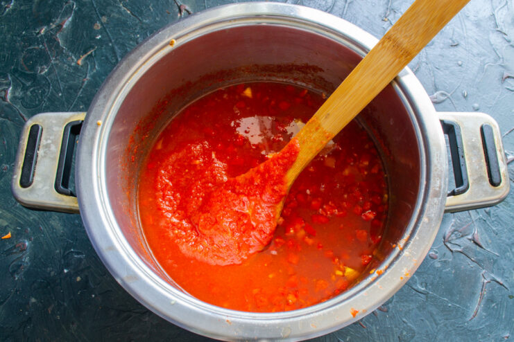 Combining Ingredients: Mixing Tomato Purée with Vegetables Smooth, sieved tomato purée being poured into a pot with chopped peppers and garlic.