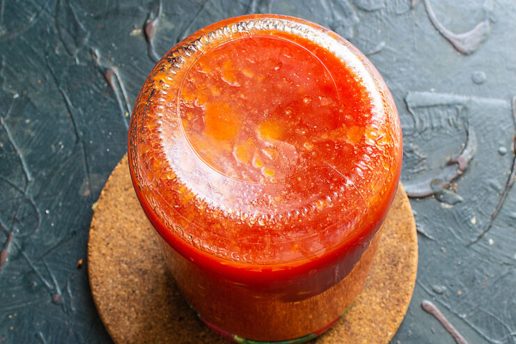 Sealing and Cooling Jars: The Final Step in Canning Sealed jars of tomato sauce turned upside down and wrapped in a thick towel to cool slowly.