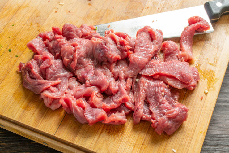 Close-up of beef fillet being sliced into thin strips on a cutting board.