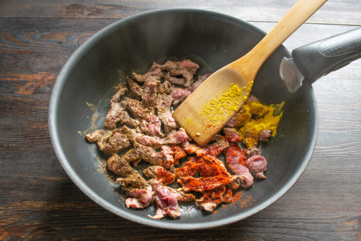 Sliced beef being seared in a hot wok, browning on all sides.