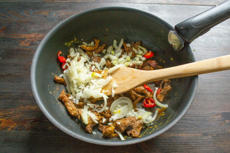 Chopped onion, garlic, and grated ginger being added to the pan with beef.