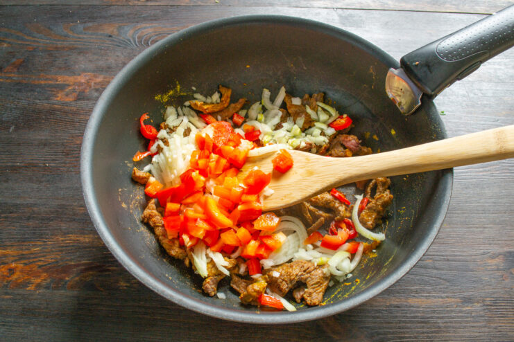 Diced red bell pepper being added to the beef and aromatics in the wok.