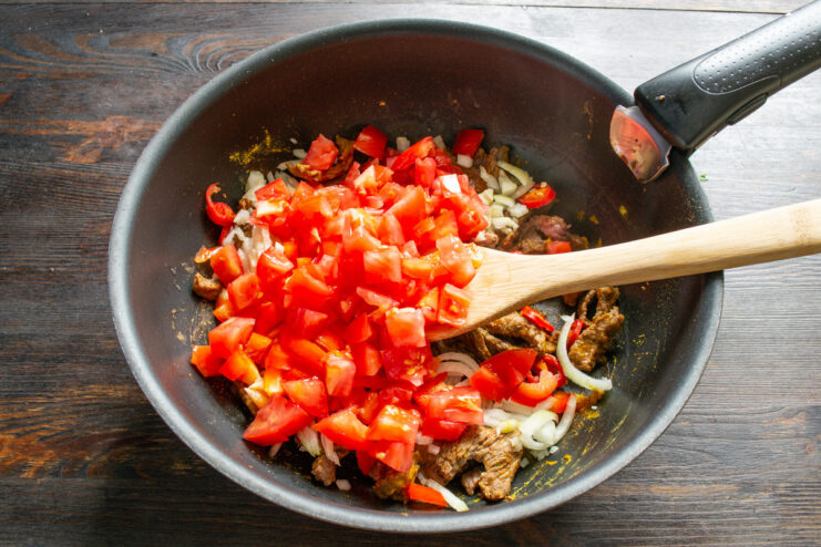 Diced fresh tomatoes being added to the pan with beef and vegetables.