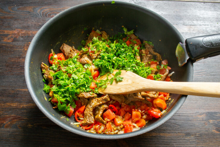 A bunch of fresh parsley and cilantro being finely chopped on a cutting board.