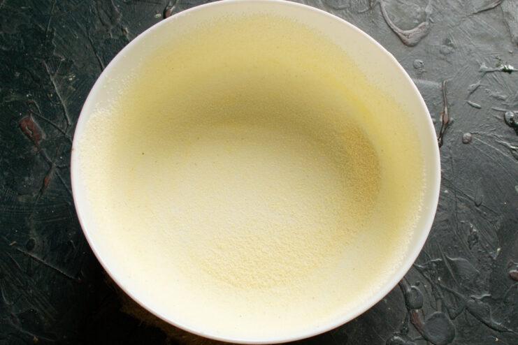 Preparing the Baking Pan for the Casserole A hand greasing a round glass baking dish with softened butter.