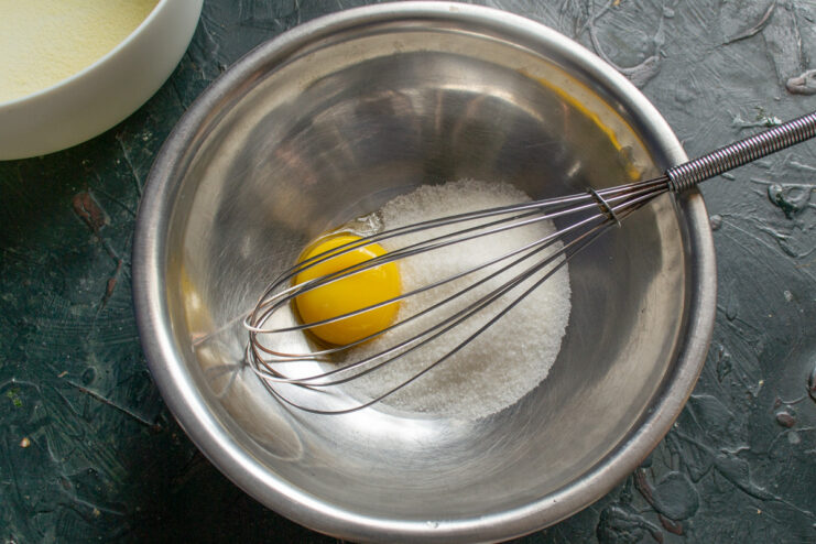 Mixing Sugar and Egg Yolk for the Casserole Batter A glass bowl containing sugar and a single egg yolk, ready for mixing.