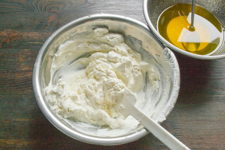 Gently folding whipped cream into the cheese mixture A spatula gently folding fluffy whipped cream into the creamy farmer's cheese mixture in a bowl.