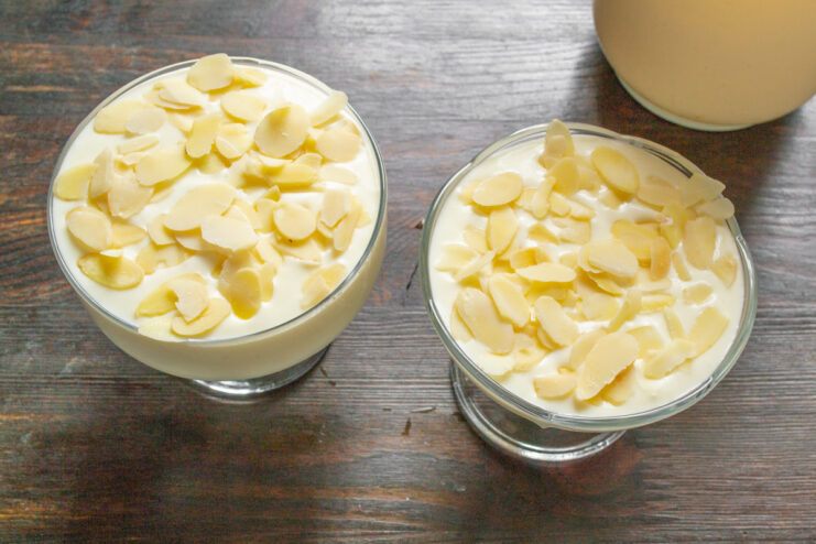 Garnishing the dessert with flaked almonds before chilling Sprinkling flaked almonds on top of the farmer's cheese dessert in glass bowls.