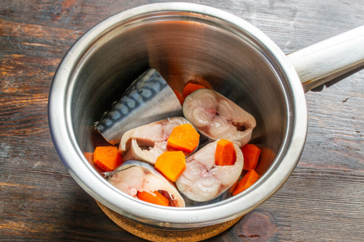 Adding Carrots to the Mackerel in a Pot Mackerel steaks and sliced carrots in a cooking pot, ready to be cooked.