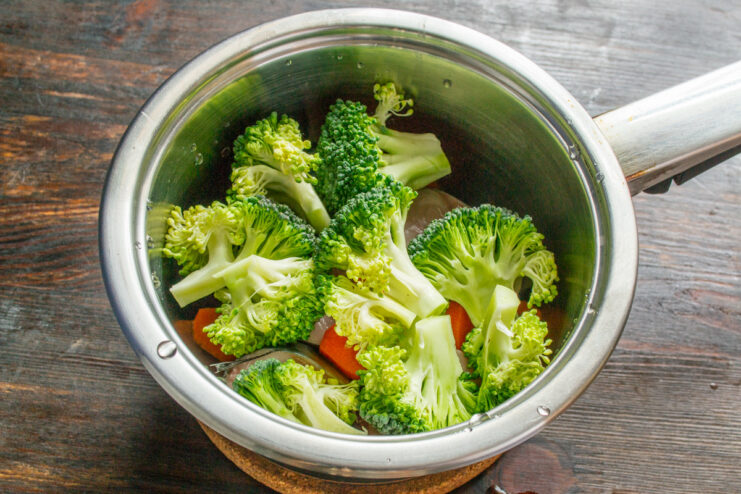Adding Broccoli to the Pot with Mackerel and Carrots Broccoli florets being added to a pot containing mackerel steaks and carrots.