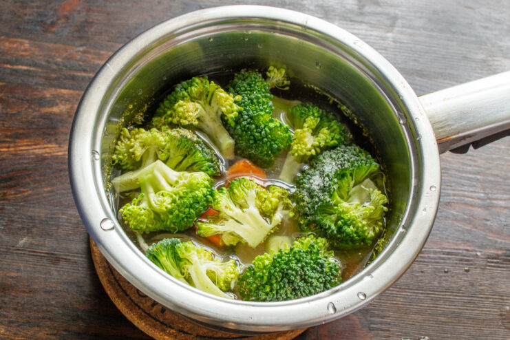 Adding Water to the Ingredients Before Boiling A pot with mackerel, carrots, and broccoli, with water being poured in to just cover the ingredients.